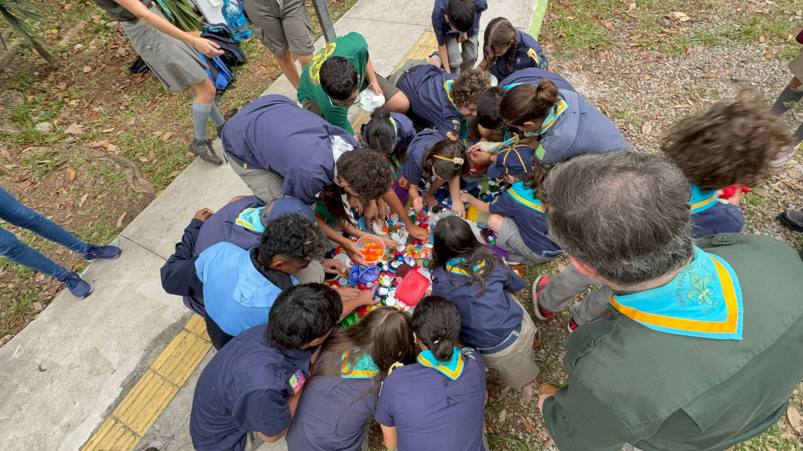 Grupo de escoteiros agachado em círculo separando tampinhas plásticas coloridas