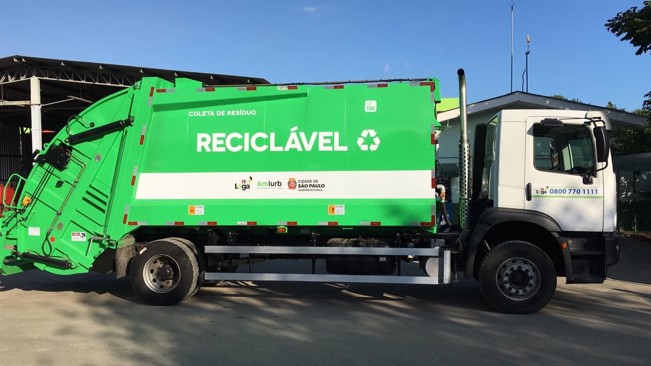 Caminhão verde da coleta seletiva recolhendo recicláveis no bairro
